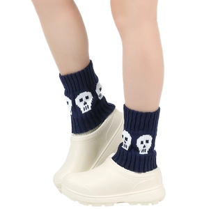 Close-up of navy blue knit leg warmers with white skull patterns on beige garden clogs
