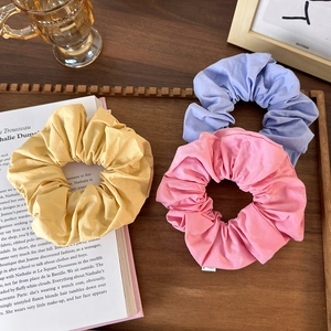 Three solid color fabric scrunchies in yellow, pink and light blue on a wooden tray
