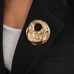 Detailed close-up of a vintage golden round brooch with hammered texture on a black blazer