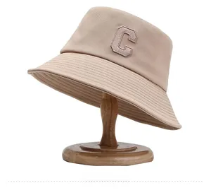 Détail d'un chapeau bob en toile beige avec logo C brodé sur un support en bois