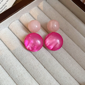 Detailed macro view of pink resin round stud earrings on a beige velvet jewelry tray