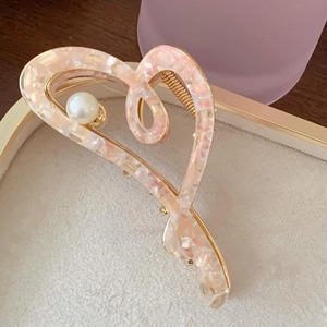 Pink heart-shaped acetate hair claw with gold metal base and pearl detail in a tray