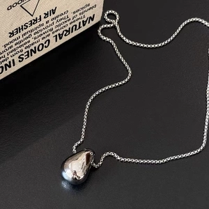 Minimalist silver teardrop pendant necklace on black leather background with vintage box