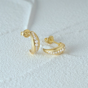 Macro shot of gold C-shaped earrings with sparkling cubic zirconia on white surface