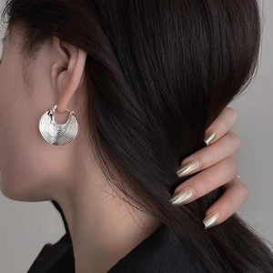 Detailed view of silver ripple textured hoop earrings worn on a female model