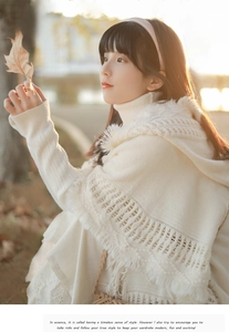Detail of off-white knitted poncho featuring textured weave patterns and fringe edges