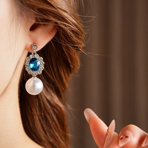 Dettaglio dell'orecchino d'argento con gemma blu e perla bianca indossato dalla modella