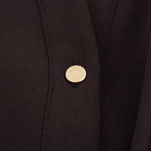 Vue macro d'un bouton doré lisse sur le tissu bordeaux texturé d'une robe chemise midi