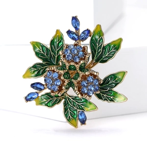 Detailed view of elegant gold flower brooch with blue crystals and green enamel leaves