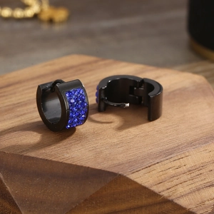 Detail of black stainless steel hoop earrings with three rows of blue rhinestones on wood