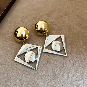 Detail of gold and silver contrast geometric rhombic earrings on beige textured background