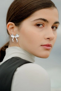 Close-up of polished silver bow stud earring worn on model against blurred background