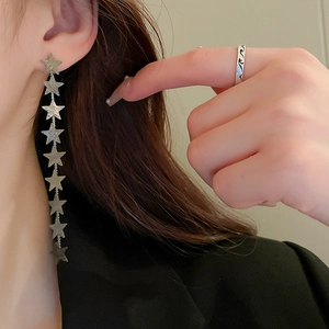 Detail of silver long tassel star earrings and a wavy ring on a female model