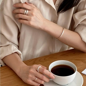 Lifestyle shot of minimalist silver 3mm square wire bracelet and rings on model holding cup