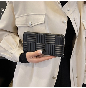 Close-up of black long wallet with woven texture and gold zipper held by a model