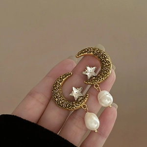 Détail de boucles d'oreilles lune dorées vintage avec gravure soleil et perle