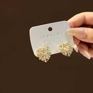 Detail of heart-shaped gold earrings with sparkling zircon crystals in hand