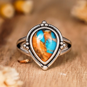 Gros plan d'une bague argentée vintage avec pierre goutte bleue et orange sur bois