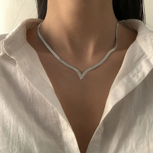 Close-up of silver-tone V-shaped snake bone fringe necklace layered on a white shirt