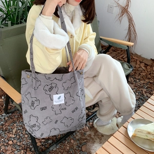 Gray corduroy tote bag with bear print shown on a model in a natural outdoor setting