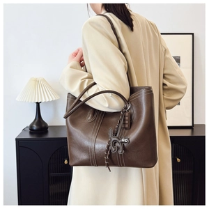 Detail of dark brown tote bag with contrast stitching and cute black cat charm on model