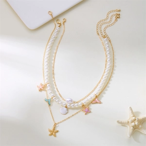Detail of layered gold necklace featuring pearl beads, pink starfish and shell pendants