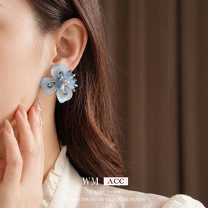Boucles d'oreilles fleurs bleues avec cristaux et perles portées sur fond marron flou