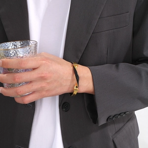 Close-up of men's C-shaped twisted steel bracelet with gold and black woven leather detail
