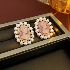 Gros plan de boucles d'oreilles camée rose avec perles et cadre doré sur support noir