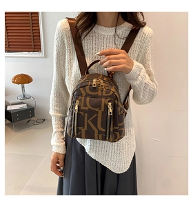 Detail of a brown leather-like mini backpack with letter patterns on a female model