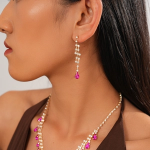Close-up of luxury gold-tone necklace and earrings set with magenta teardrop crystals