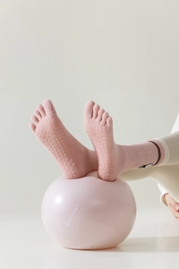 Pink five-toe yoga socks with anti-slip grip soles and striped cuffs on a yoga ball