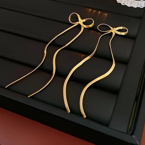 Détail des boucles d'oreilles nœud plaquées or avec de longues chaînes serpent sur plateau