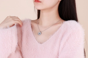 Macro view of silver Pisces zodiac pendant on a snake chain worn with a pink sweater