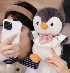 Close-up of cute penguin plush toy with pink silk bow and pearl, being held by person