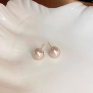Détail de boucles d'oreilles perles roses sur un plateau décoratif en coquillage