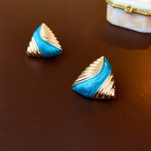 Macro detail of triangle vintage earrings featuring gold texture and blue enamel finish