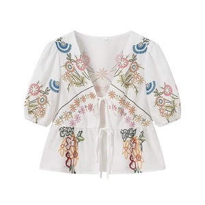 Detail of white puff sleeve blouse featuring delicate floral embroidery and V-neck tie