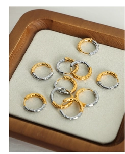 Close-up of small U-shaped hoop earrings with hammered gold and silver finish texture