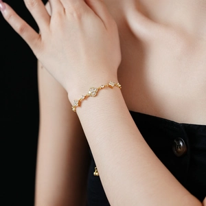 Close-up of gold-plated bracelet with diamond-encrusted clover pendants on a wrist