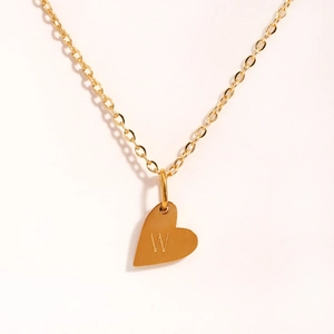 Vue détaillée d'un pendentif cœur doré avec la lettre W gravée sur une chaîne en acier
