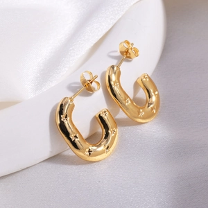 Close-up of golden U-shaped earrings with star pattern engraving on white silk