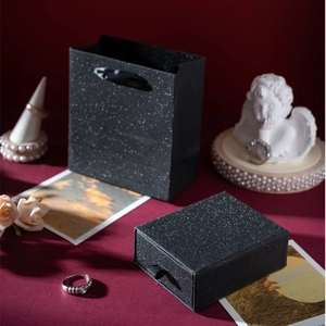 Close-up of black glitter jewelry gift box with matching bag on dark red velvet surface