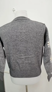 Close-up of white and yellow daisy embroidery on grey knitted long sleeve cardigan