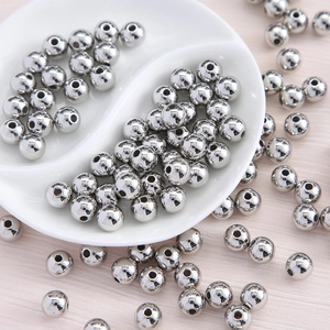 Close-up of polished silver acrylic round beads for DIY jewelry making on white ceramic tray