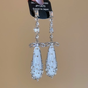 Detail of silver bow earrings with elegant white teardrop pendants and crystal accents