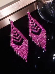 Close-up of pink rhinestone tassel earrings with geometric hollow design on black surface