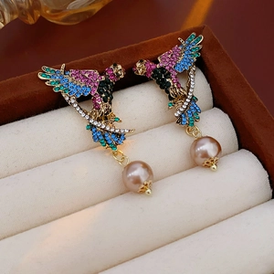 Close-up of vintage parrot earrings with colorful rhinestones and pink pearls in a box
