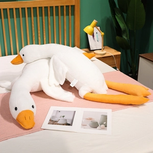 Detail of soft white goose plush pillow with orange beak and feet on a cozy bed