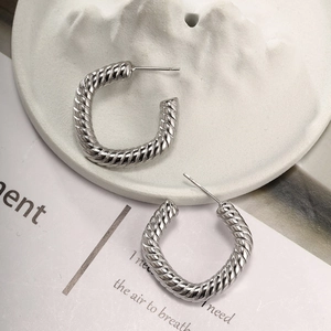 Macro detail of silver C-shaped twisted rope earrings on a white marble display tray
